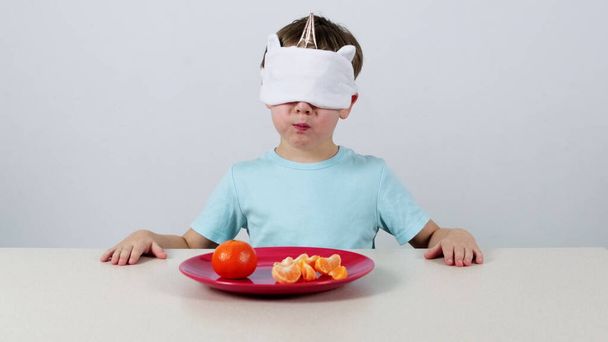 Kleine jongen met een masker probeert en raadt mandarijn - Foto, afbeelding