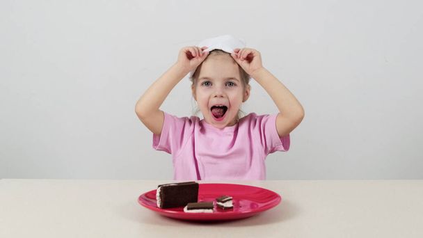 Klein meisje in een masker probeert en raadt chocolade taart met witte room - Foto, afbeelding