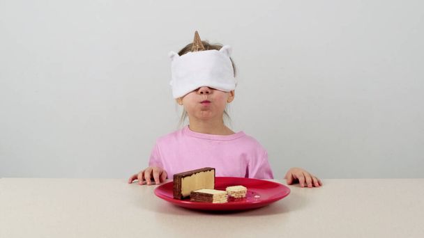Klein meisje in een masker probeert en raadt wafels met chocolade - Foto, afbeelding