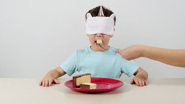 Kleine jongen in een masker probeert en raadt wafels met chocolade en geeft duimen omhoog - Foto, afbeelding
