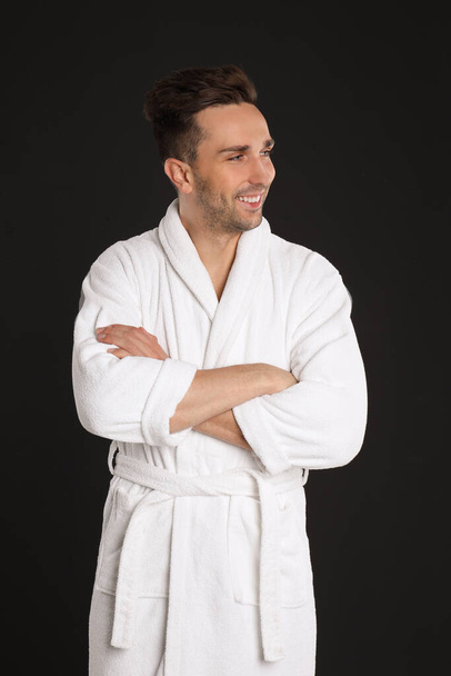 Happy young man in bathrobe on black background - Foto, afbeelding
