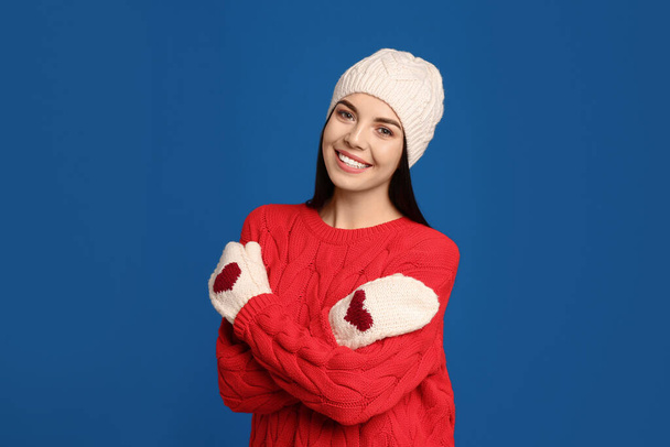 Young woman wearing warm sweater, mittens and hat on blue background. Winter season - Valokuva, kuva