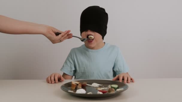 Ένα αγόρι με μαύρη μάσκα προσπαθεί να μαντέψει μια ποικιλία φαγητών. - Πλάνα, βίντεο