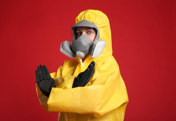 Woman in chemical protective suit making stop gesture on red background. Virus research - Foto, Imagen
