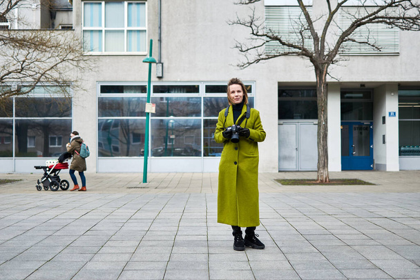 Vienna, Austria - March 11, 2020: Woman tourist in a green coat with a camera on a city street. - Photo, Image