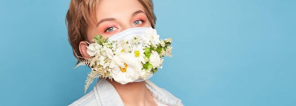 Face mask design with flowers. Portrait of beautiful woman with blue eyes, fashion make-up and mask over blue wall - Photo, Image