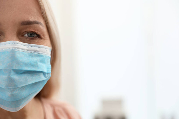 Mature woman wearing medical mask at home, closeup view with space for text. Dangerous virus - Foto, imagen