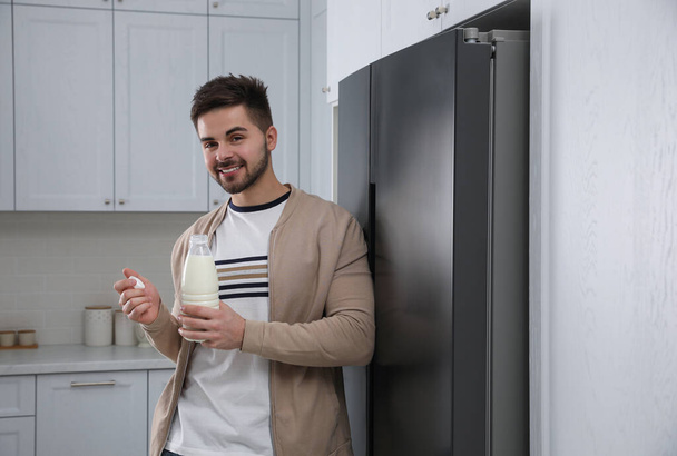 Young man with bottle of milk near refrigerator in kitchen - Photo, Image