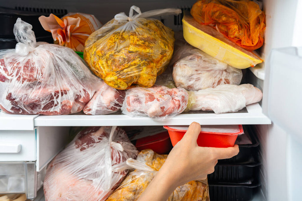 Una mujer saca y pone comida congelada en un congelador para un almacenamiento prolongado
. - Foto, imagen