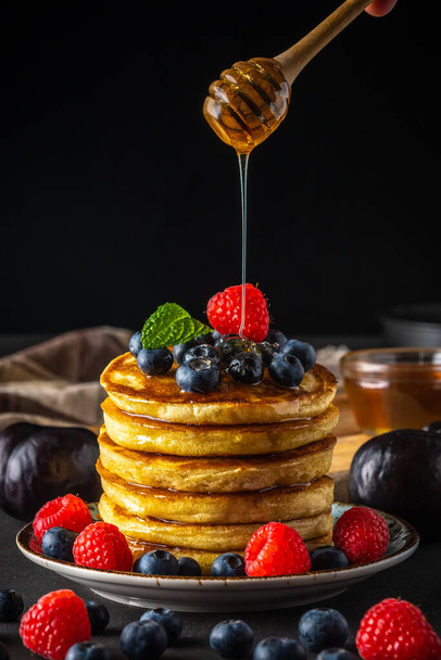 Delicious pancakes with fresh berries and dripping honey on dark background. Food concept. - Fotoğraf, Görsel