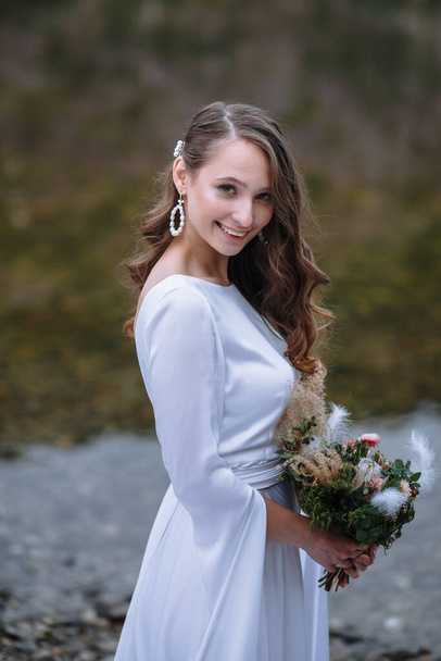 A bride in a long wedding dress standing on the shore of a lake - Foto, Imagen