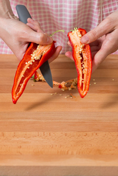 Close-up van de handen pellen en rode paprika 's snijden op een houten plank. Gezond voedselbereidingsconcept - Foto, afbeelding