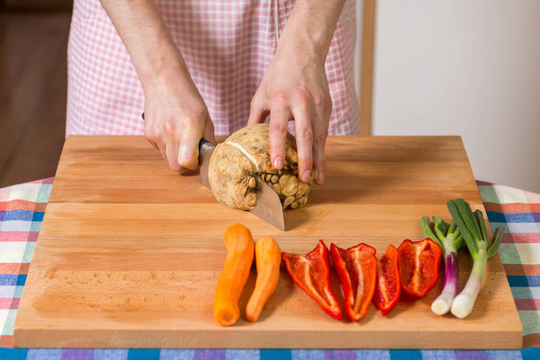 Close up of hands peeling and cutting celery root on a wooden board. Healthy food preparation concept - Photo, image