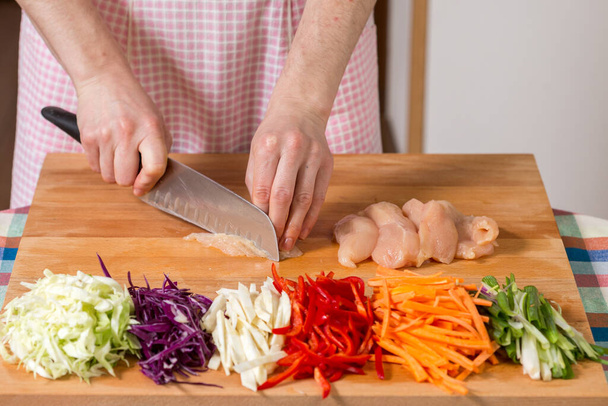 Feche de mãos que cortam o peito de frango em uma tábua de madeira. Conceito de preparação alimentar saudável
 - Foto, Imagem