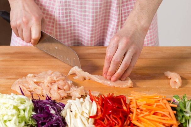 Sluiten van handen snijden kippenborst op een houten plank. Gezond voedselbereidingsconcept - Foto, afbeelding