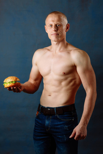 Спортивный спортсмен с гамбургером. Нездоровое питание или спорт, выбор образа жизни. Концепция нездорового питания
. - Фото, изображение