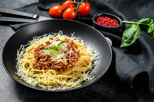 Makaron bolognese spaghetti z pomidorem i mięsem mielonym, serem parmezanowym i bazyliką. Czarne tło. Widok z góry. - Zdjęcie, obraz
