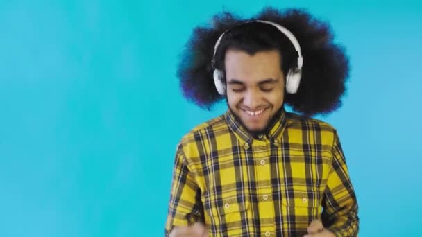 Θετικός Αφροαμερικάνος ακούει μουσική με τα ακουστικά του σε μπλε φόντο. Έννοια των συναισθημάτων - Πλάνα, βίντεο