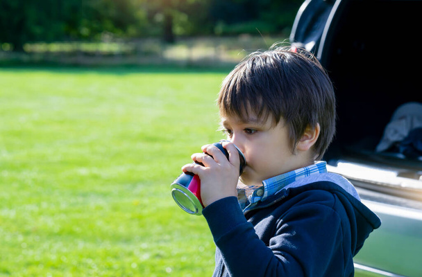 Portret van Happy boy naast een auto drinken frisdrank met een vrolijk gezicht, Actieve kind jongen reizen met de auto met ouders tijdens de schoolvakantie in de zomer, Kid drinken frisdrank. - Foto, afbeelding