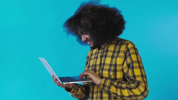 Αφροαμερικάνος δακτυλογραφεί στο λάπτοπ και χαμογελάει σε μπλε φόντο. Έννοια των συναισθημάτων - Πλάνα, βίντεο