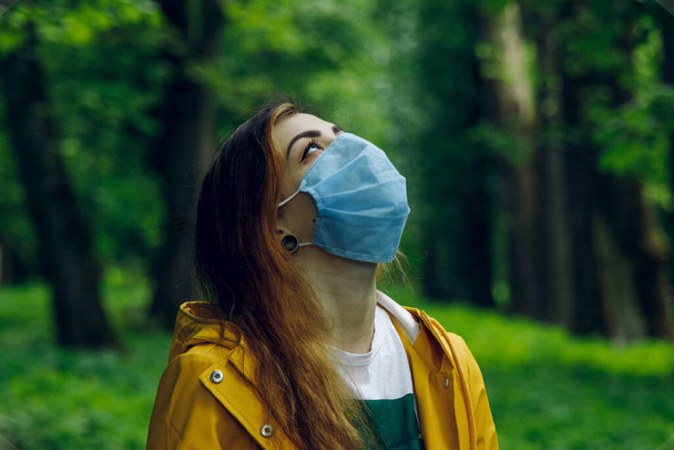 female portrait in mask wish to breathe by clean air and looking on nature, actual pollution and corona virus concept - Photo, Image