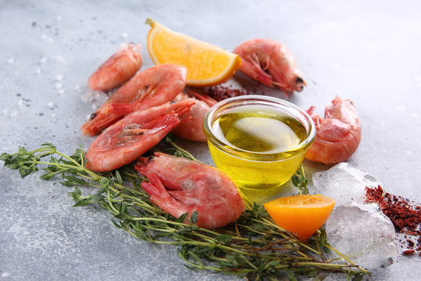 Seafood. Raw pink prawns shrimp on a white wooden board with lemon, thyme, tomato, spices and ice on a light grey background. Background image, copy space  - Photo, image