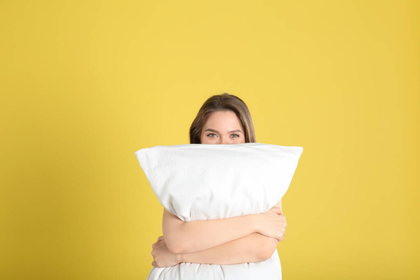Young woman with pillow on yellow background - Фото, зображення