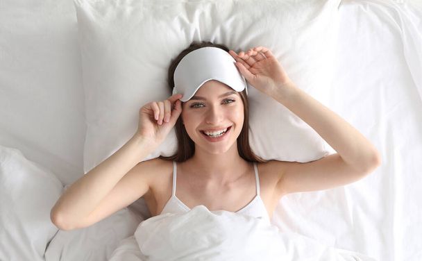 Young woman with sleep mask lying on comfortable pillow in bed at home, top view - Foto, immagini