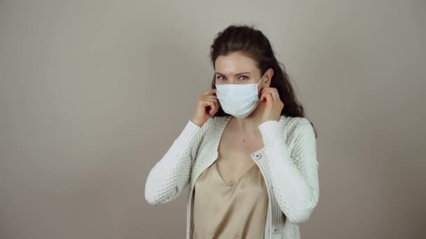 Brunette young woman take off protective mask on face in coronavirus pandemic on grey background. - Footage, Video