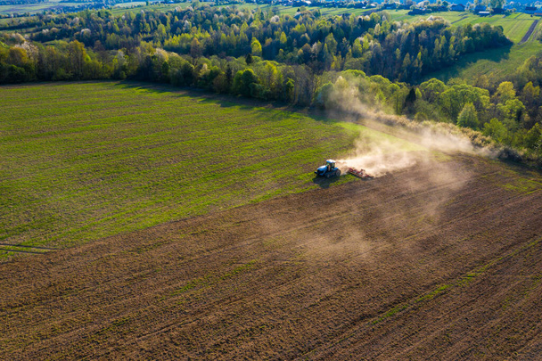 Фермер культивує поле на гусеничному тракторі і звільняє ґрунт за допомогою дискового культиватора на тлі лісового та блакитного неба 2021
. - Фото, зображення