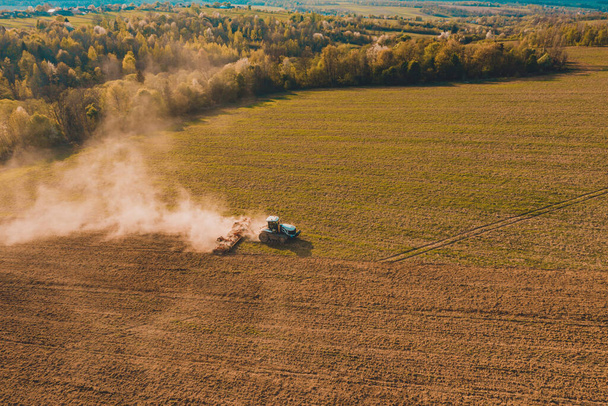 Πλευρική όψη αεροσκάφους που ίπταται πάνω από αγρό που καλλιεργείται από ερπυστριοφόρο ελκυστήρα κατά τη διάρκεια κρίσης στον γεωργοβιομηχανικό τομέα 2020 - Φωτογραφία, εικόνα