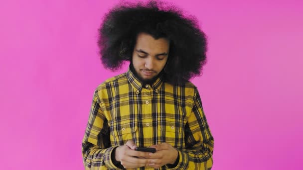 Молодой красивый африканский американец пользуется телефоном на фиолетовом фоне. Концепция эмоций
 - Кадры, видео