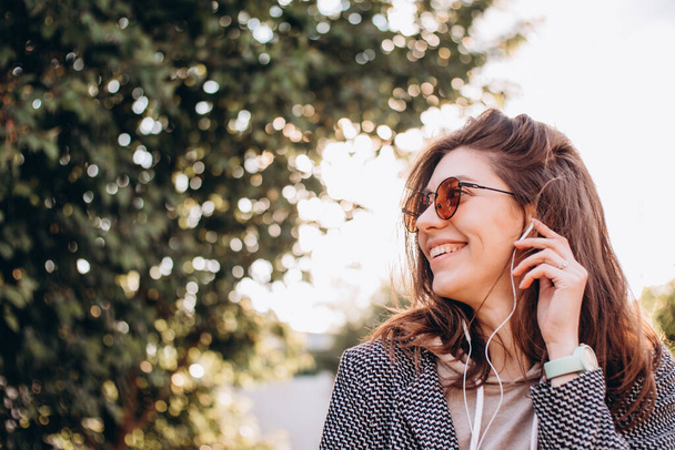 zbliżenie portret pięknej młodej kobiety z uśmiechem słucha i cieszy się muzyką z telefonu w słuchawkach w parku - Zdjęcie, obraz