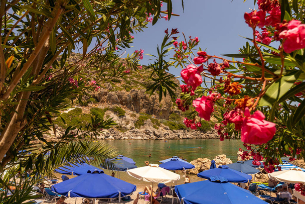 Rhodes, Greece - July 5, 2019 - In a bay on the beautiful island of Rhodes, holidaymakers relax under parasols - Photo, Image