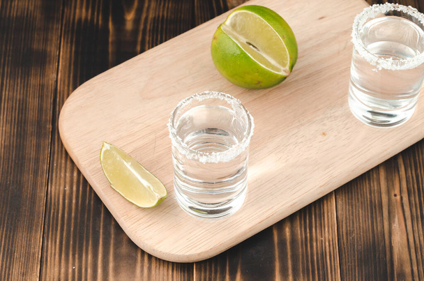 two Tequila shots with lime slices and salt on wooden table/Tequila shots and lime slice on wooden table. Top view. - Photo, Image