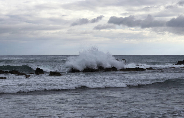 Viharfelhők közelednek, és velük együtt erős szél is, ami hatalmas számú közepes hullámot hozott, ami folyamatosan lezuhan a sziklás sziklákon. A tengerek és az óceán uralma. Veszélyes helyzet. - Fotó, kép