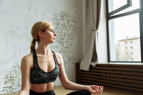 Giovane donna sana e bella seduta a casa in posizione yoga. Una bella ragazza è impegnata nella meditazione a casa in un interno luminoso
. - Foto, immagini
