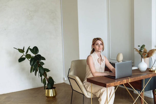 若い美しい女性は、フリーランスとして机の上にラップトップを持つ家庭からコンピュータのために働く. - 写真・画像