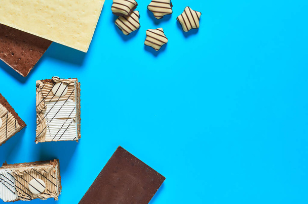 Three rectangular pieces of cake beside different chocolate bars and candies in form of stars lies on blue table on party. Celebration concept. Space for text. Top view - Foto, imagen