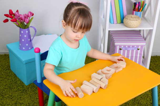 Little girl plays with construction blocks sitting at table in room - Φωτογραφία, εικόνα
