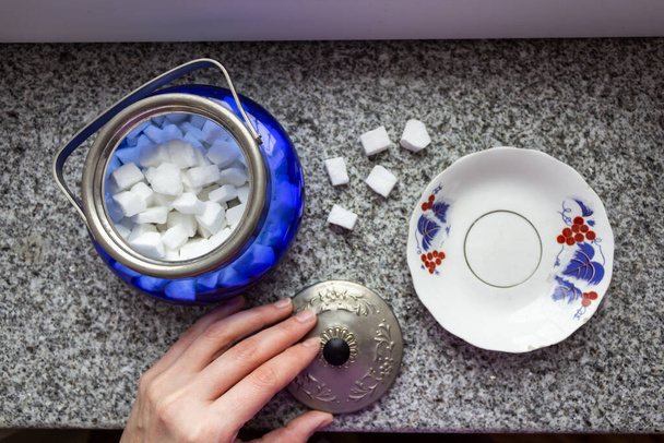 A mão feminina segura uma tigela de açúcar na qual se encontra o açúcar branco
 - Foto, Imagem