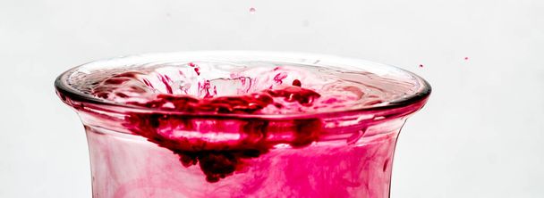 gotas de água vermelha caindo em um copo com água transparente, com um fundo branco
. - Foto, Imagem