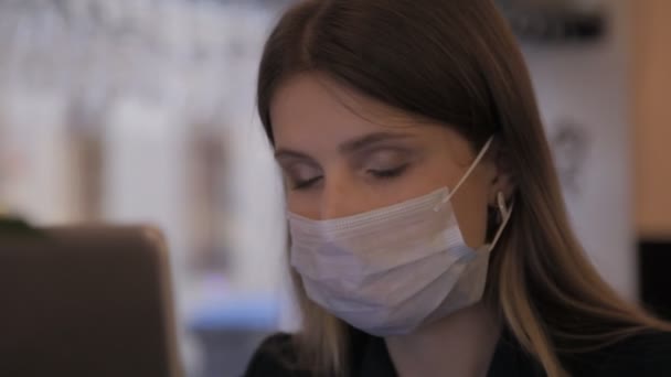 Girl of Slavic appearance in medical mask and rubber gloves works at computer-laptop. Woman removes her mask and smiles. Close-up (face) of young female. Concept of working during Covid-19 pandemic - Filmmaterial, Video