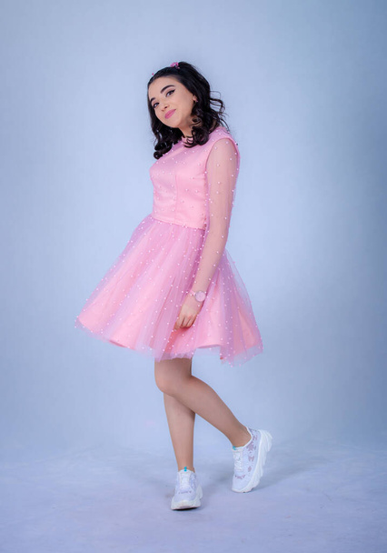 Portrait Of Beautiful Young girle Standing Against blue Background,girl in a pink dress,Happy cheery smiling young cute girl posing isolated,White running shoes, - Zdjęcie, obraz
