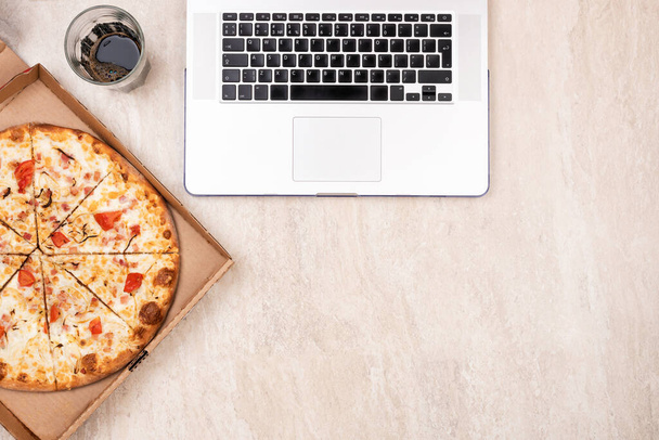 Pizza in a cardboard box and laptop on a light marble background. Copy space for your text. Top view, flat lay. Takeaway food concept - Φωτογραφία, εικόνα