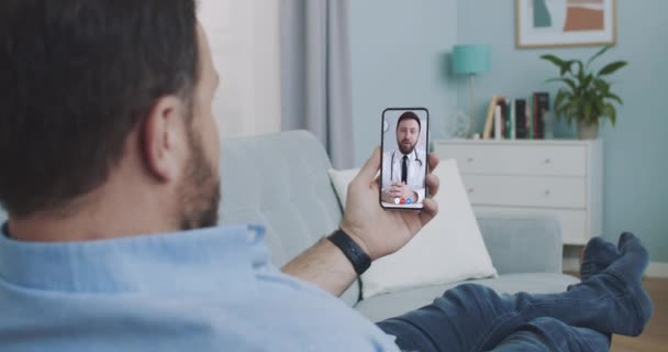Man using medical app on smartphone consulting with doctor via video conference. Male using online chat to talk with family therapist and checks possible symptoms during pandemic of coronavirus - Filmagem, Vídeo