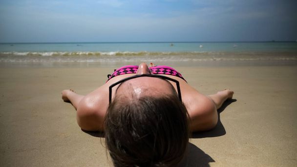 дівчина лежить на мокрій пляжі проти хвиль, що котиться на узбережжі океану
 - Фото, зображення