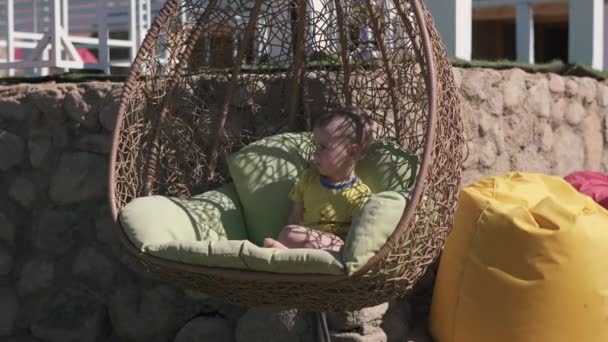 Μικρό παιδί κάθεται και ταλαντεύεται σε μια κούνια λυγαριά το καλοκαίρι σε slo-mo - Πλάνα, βίντεο