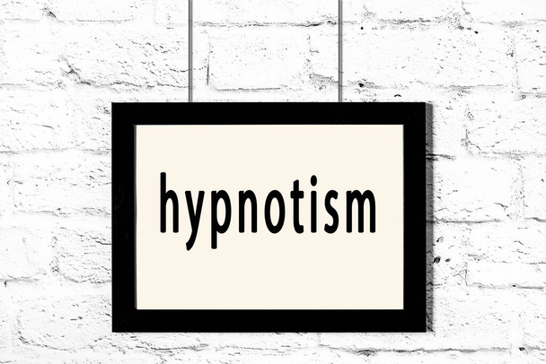 Czarna ramka wisząca na białej ceglanej ścianie z napisem hipnoza - Zdjęcie, obraz