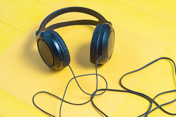 wooden background in yellow retro style. On it are black headphones and part of the wire. - Photo, Image